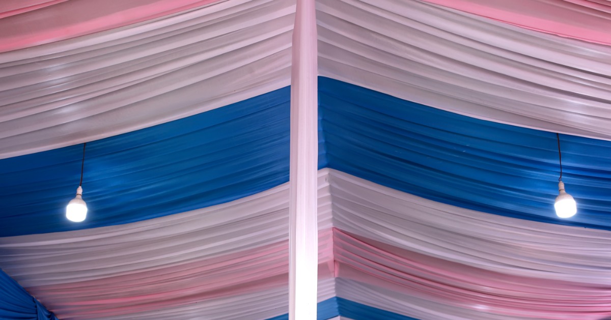 A tall ceiling decorated with sheer voile drapery in various colors. The drape colors include pink, white, and blue.